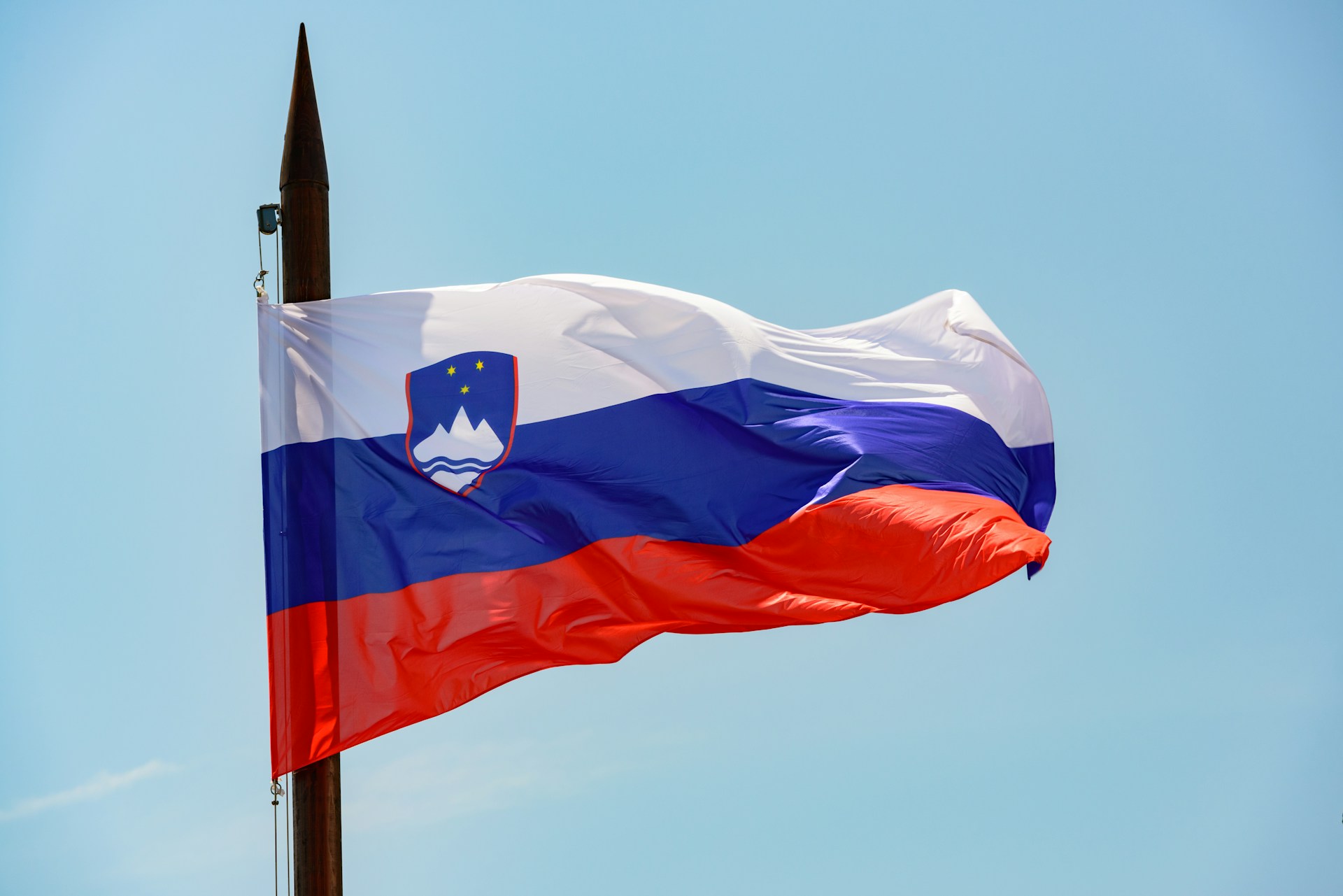 Slovenian lippu, jossa on valkoinen, sininen ja punainen raita sekä vaakuna tangon puolella